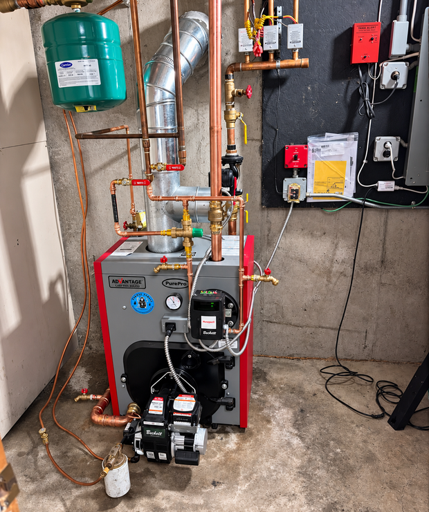 Boiler and plumbing equipment in a utility room, with pipes, gauges, pumps, and a green expansion tank.