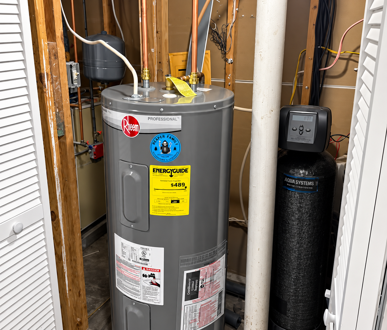 Gray water heater in a utility closet with pipes, a yellow warning label, and a water softener tank.