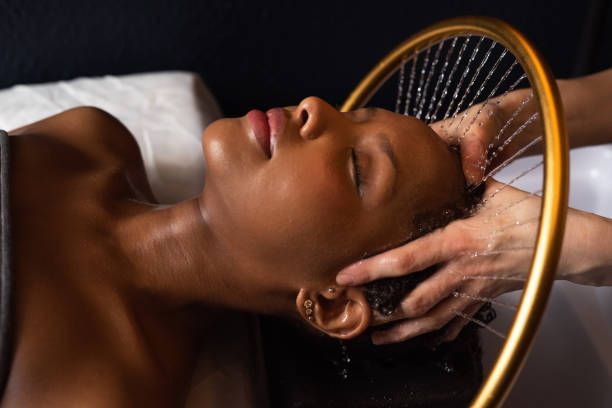 Person lying back with shampoo lather in hair at a salon sink, eyes closed