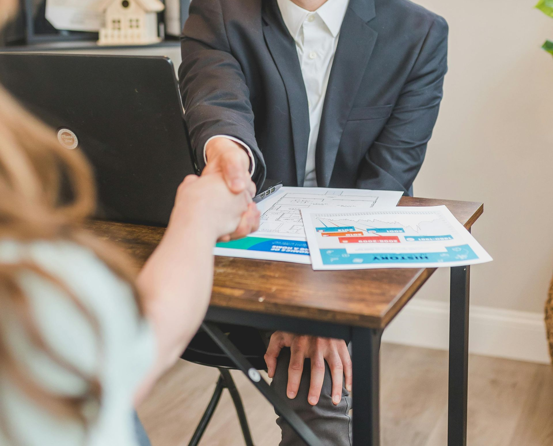 Business meeting handshake over desk with charts and laptop in the background