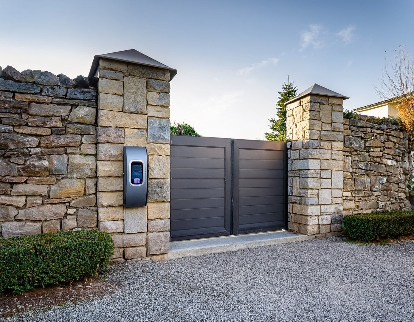 Stone gate entrance with dark gray wooden double gates, EV charger.
