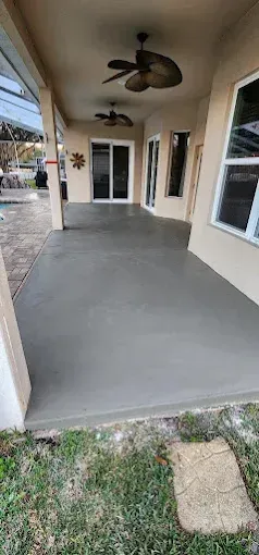 A newly poured concrete patio with two ceiling fans. A sliding door and windows are visible.