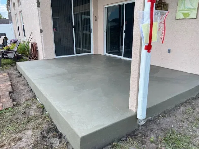 Newly poured concrete patio outside a house with sliding glass doors and a downspout.