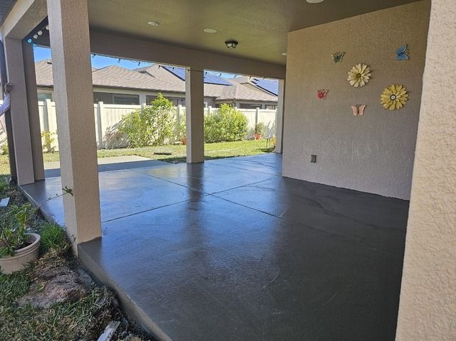 Covered patio with gray concrete floor, open to a backyard. Decorative flowers on wall. Covered patio with gray concrete floor, open to a backyard. Decorative flowers on wall.