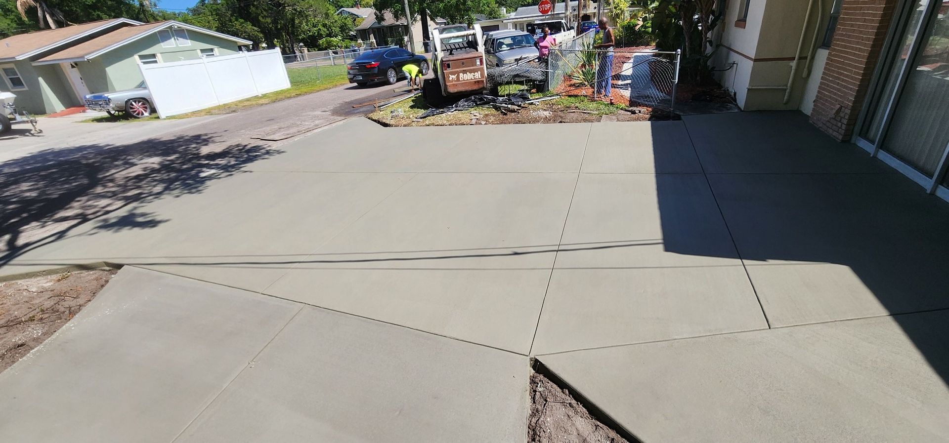 Freshly poured concrete driveway with a street and houses in the background. Construction vehicles are present. Freshly poured concrete driveway with a street and houses in the background. Construction vehicles are present.