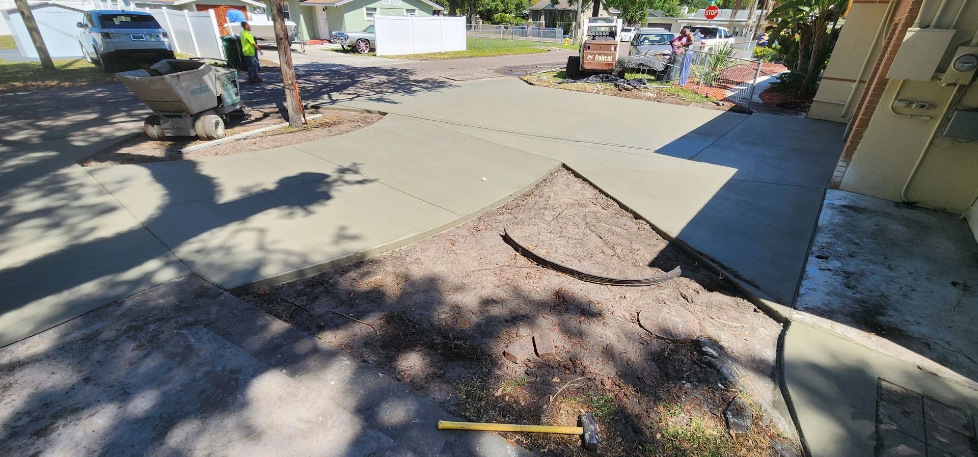 Workers pouring concrete on a driveway, with construction equipment and a partially paved area. Workers pouring concrete on a driveway, with construction equipment and a partially paved area.
