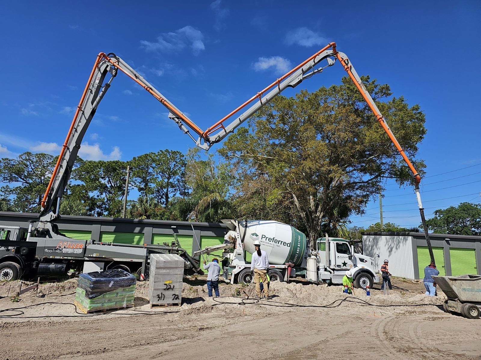 Construction site with a concrete pump truck extending over workers, pouring concrete. Sunny day, blue sky. Construction site with a concrete pump truck extending over workers, pouring concrete. Sunny day, blue sky.