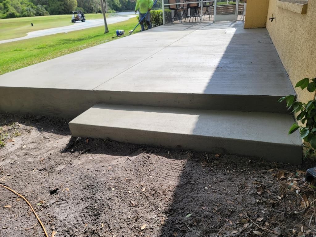 Newly poured concrete patio with steps leading to a yard, near a golf course. A worker is trimming grass. Newly poured concrete patio with steps leading to a yard, near a golf course. A worker is trimming grass.