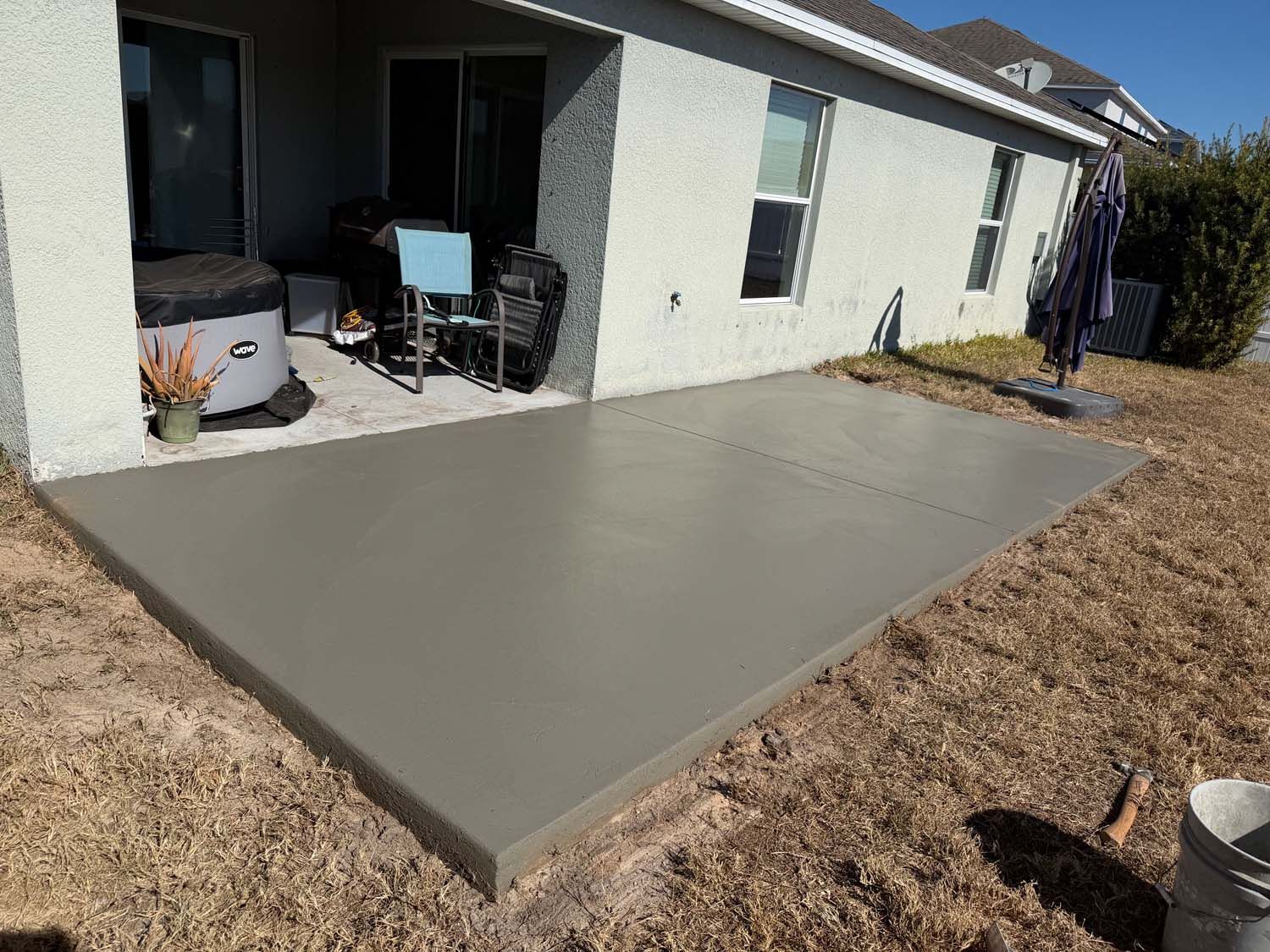 Newly poured concrete patio next to a house with an outdoor seating area.