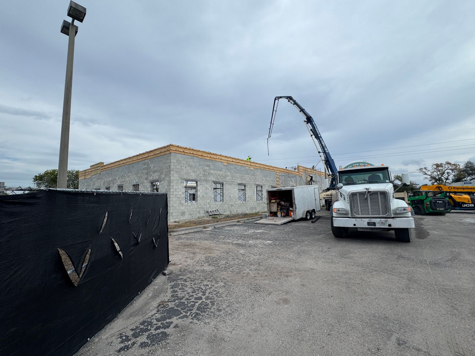 Construction site: Concrete truck, pump in use, partially built block building, overcast sky.