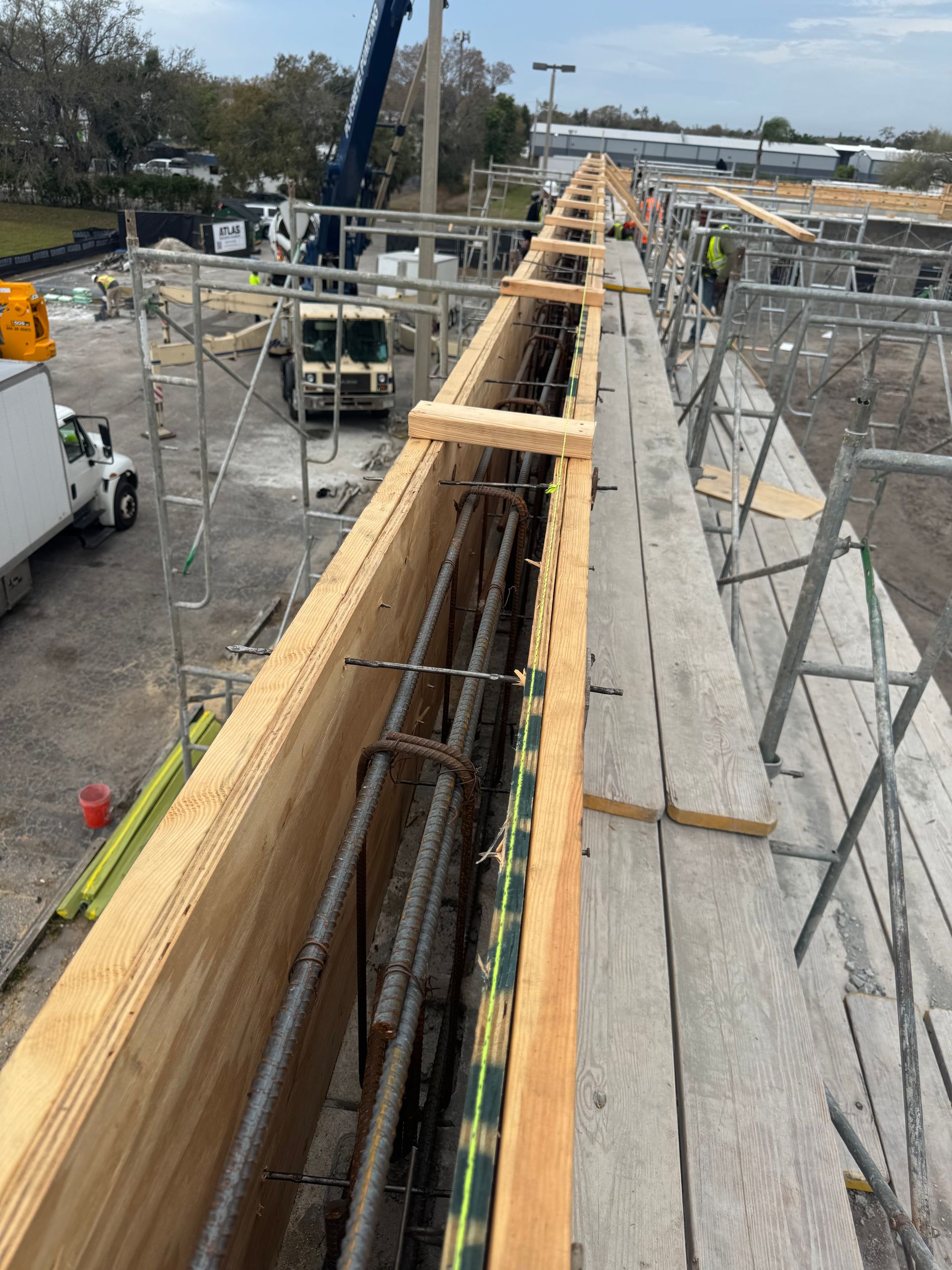 Construction site: Wooden formwork with steel reinforcement for concrete structure; crane and scaffolding present.