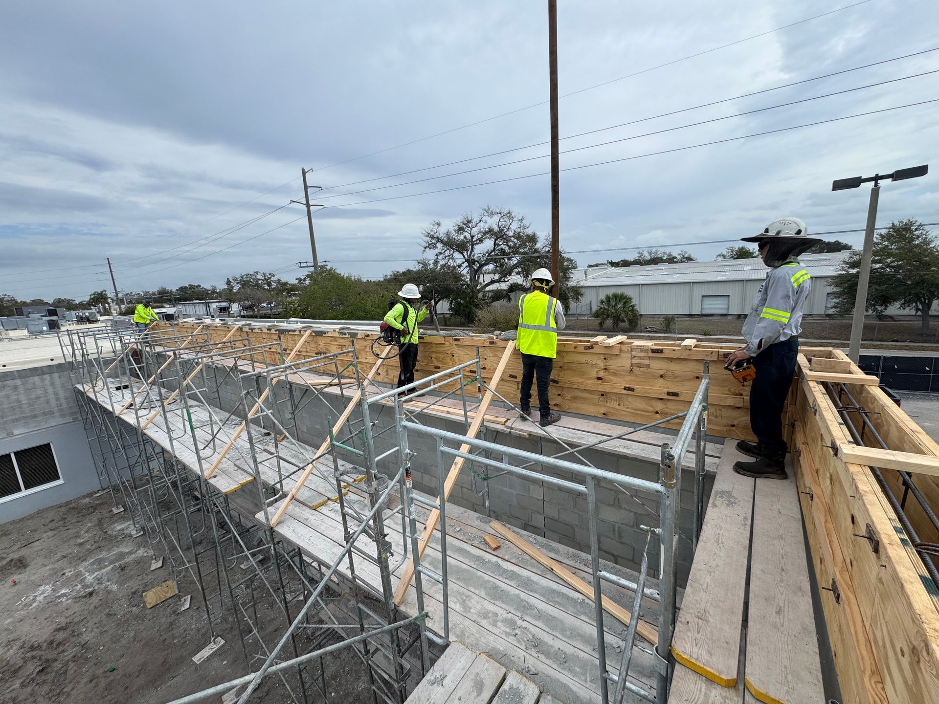 Construction workers on a rooftop, building with wood and concrete. Scaffolding, safety vests, cloudy sky.