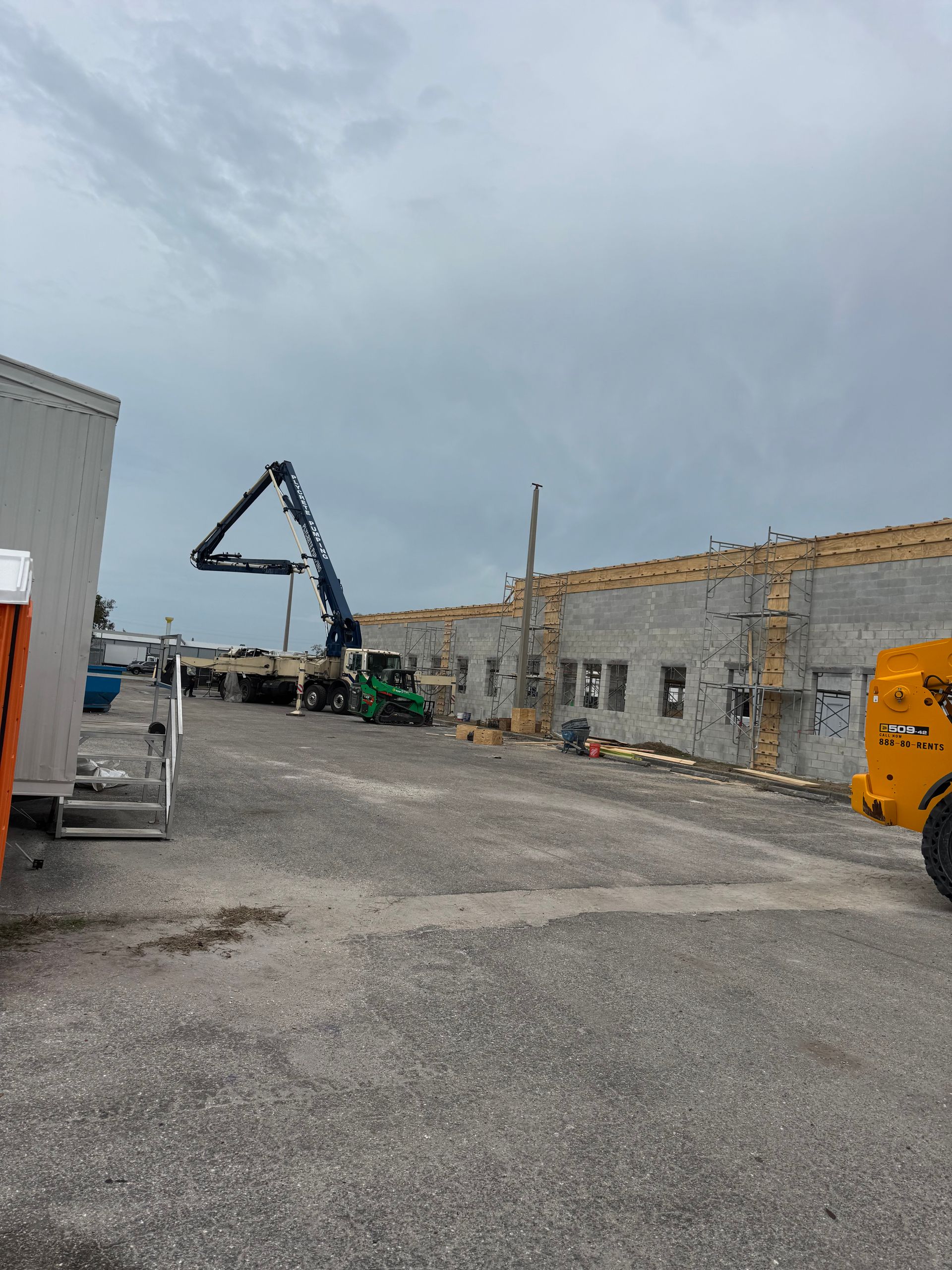 Construction site: Concrete pump pouring concrete onto a building with cinder block walls under an overcast sky.