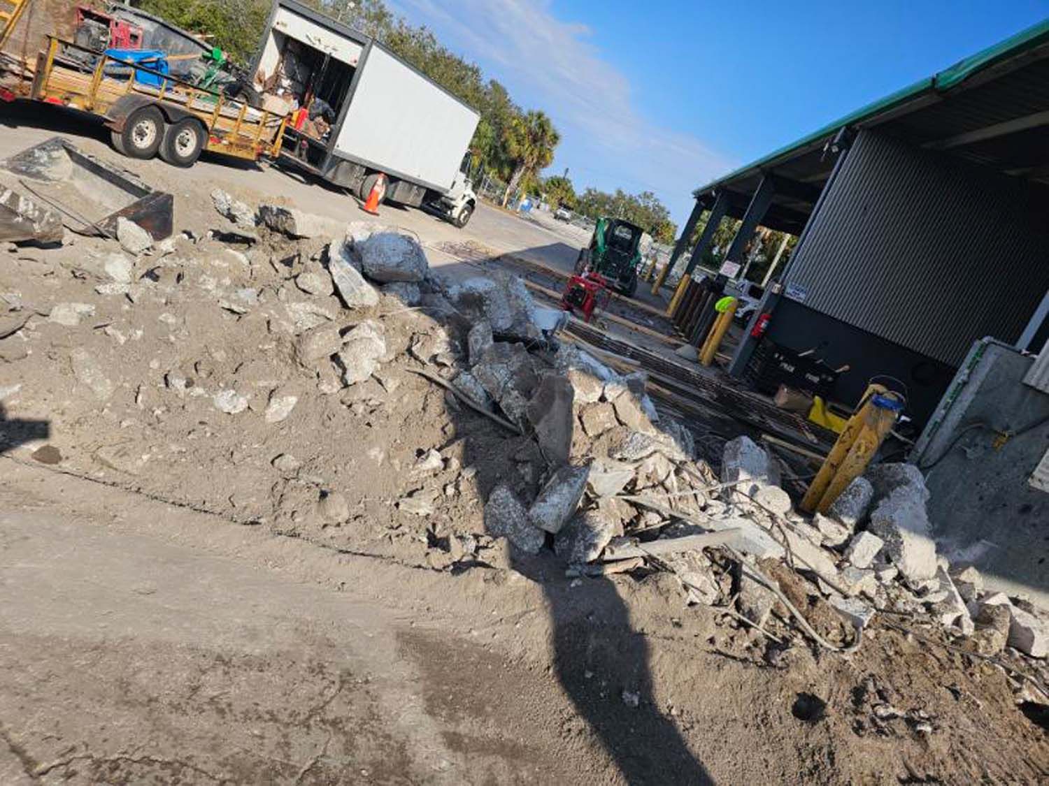 Construction site with debris on a road. Truck, trailer, and workers near a building.