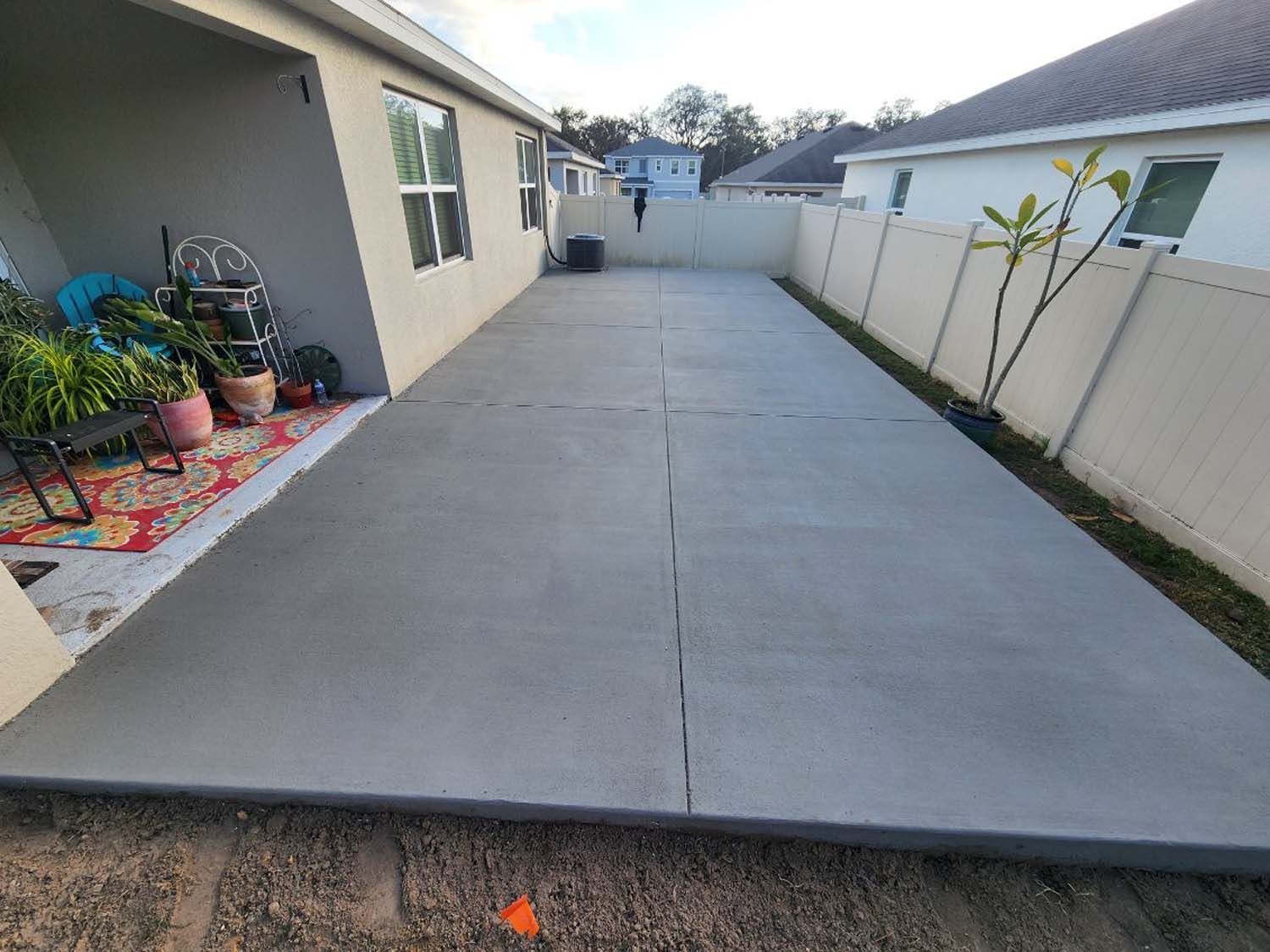 Concrete patio next to a house with a white fence and a few plants.