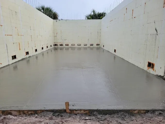 Newly poured concrete floor within beige insulated concrete form walls.