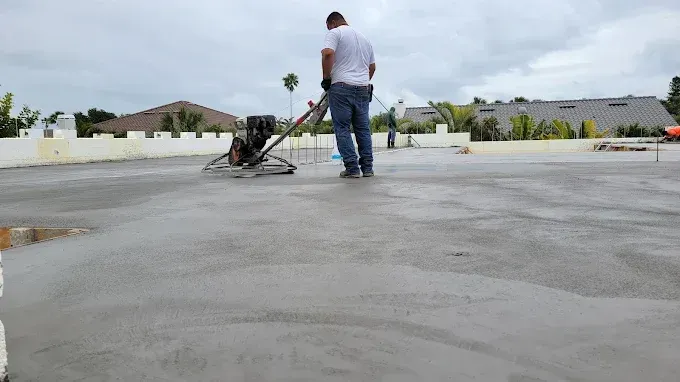 A worker smoothing wet concrete with a power trowel on a flat surface outdoors.