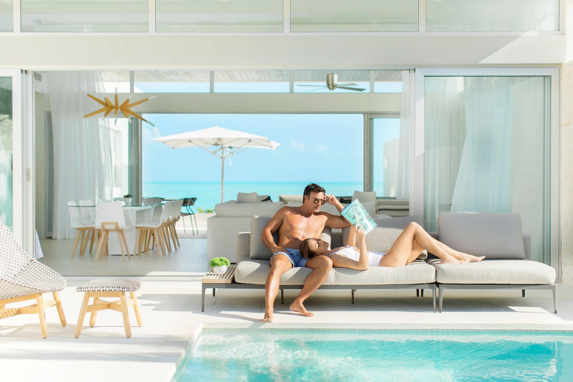 A man and woman sit on a couch next to a pool