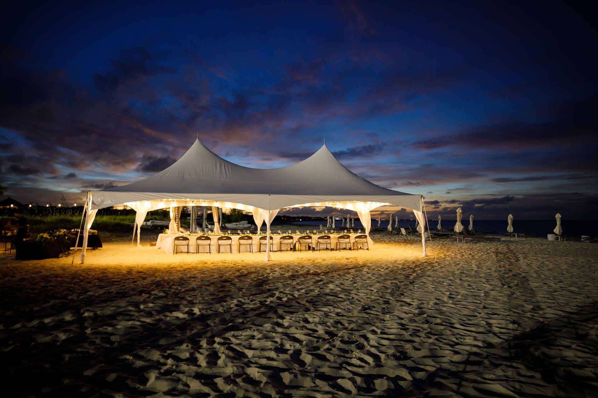 A white tent is lit up on the beach at night
