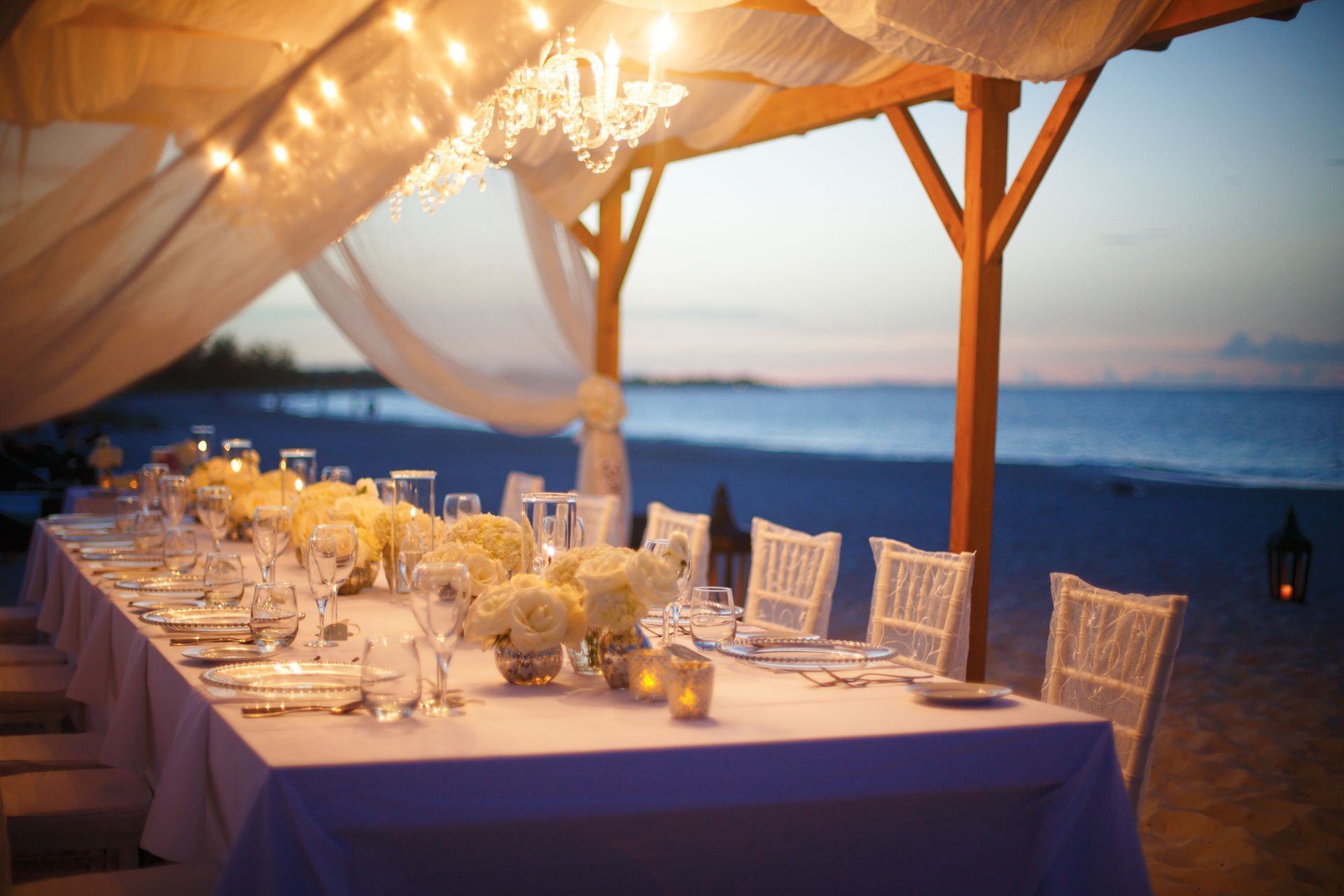 A long table is set up on the beach under a canopy