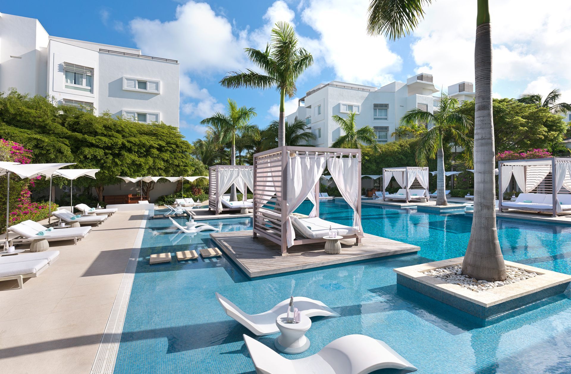 A large swimming pool surrounded by white buildings and palm trees