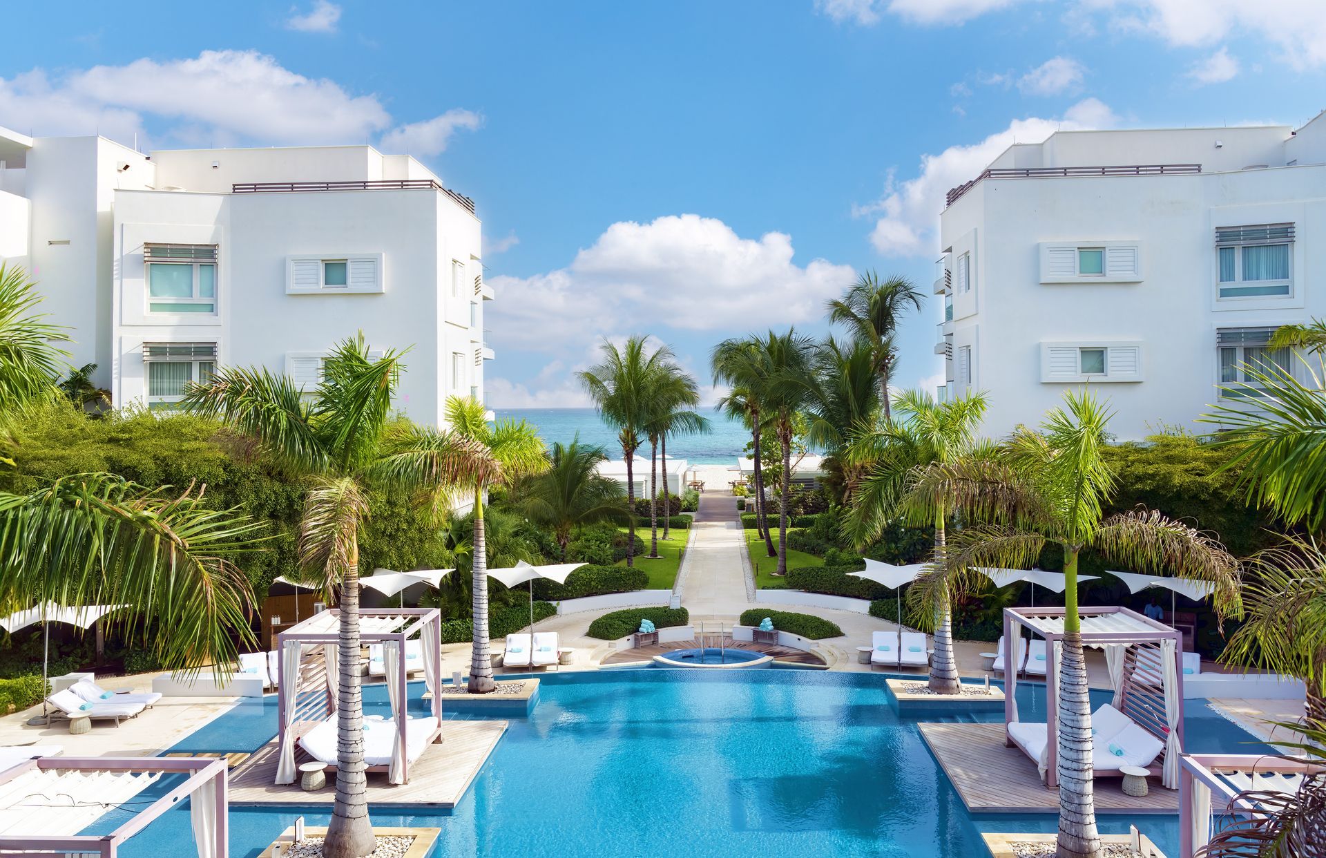 A large swimming pool surrounded by white buildings and palm trees at Wymara Resort + Villas, Turks and Caicos