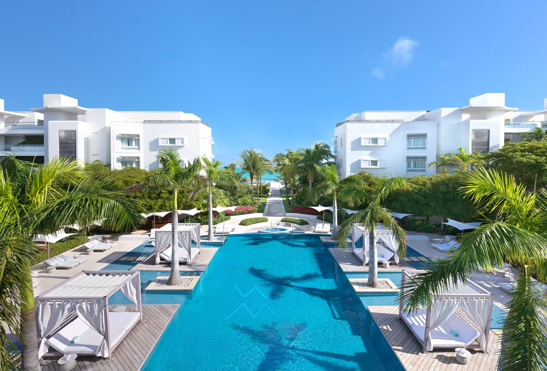 A large swimming pool surrounded by white buildings and palm trees