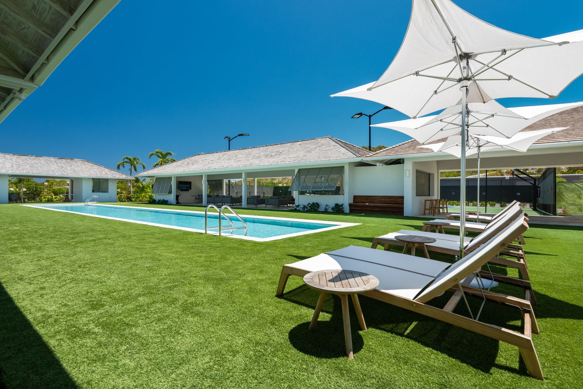 A large swimming pool is surrounded by lawn chairs and umbrellas