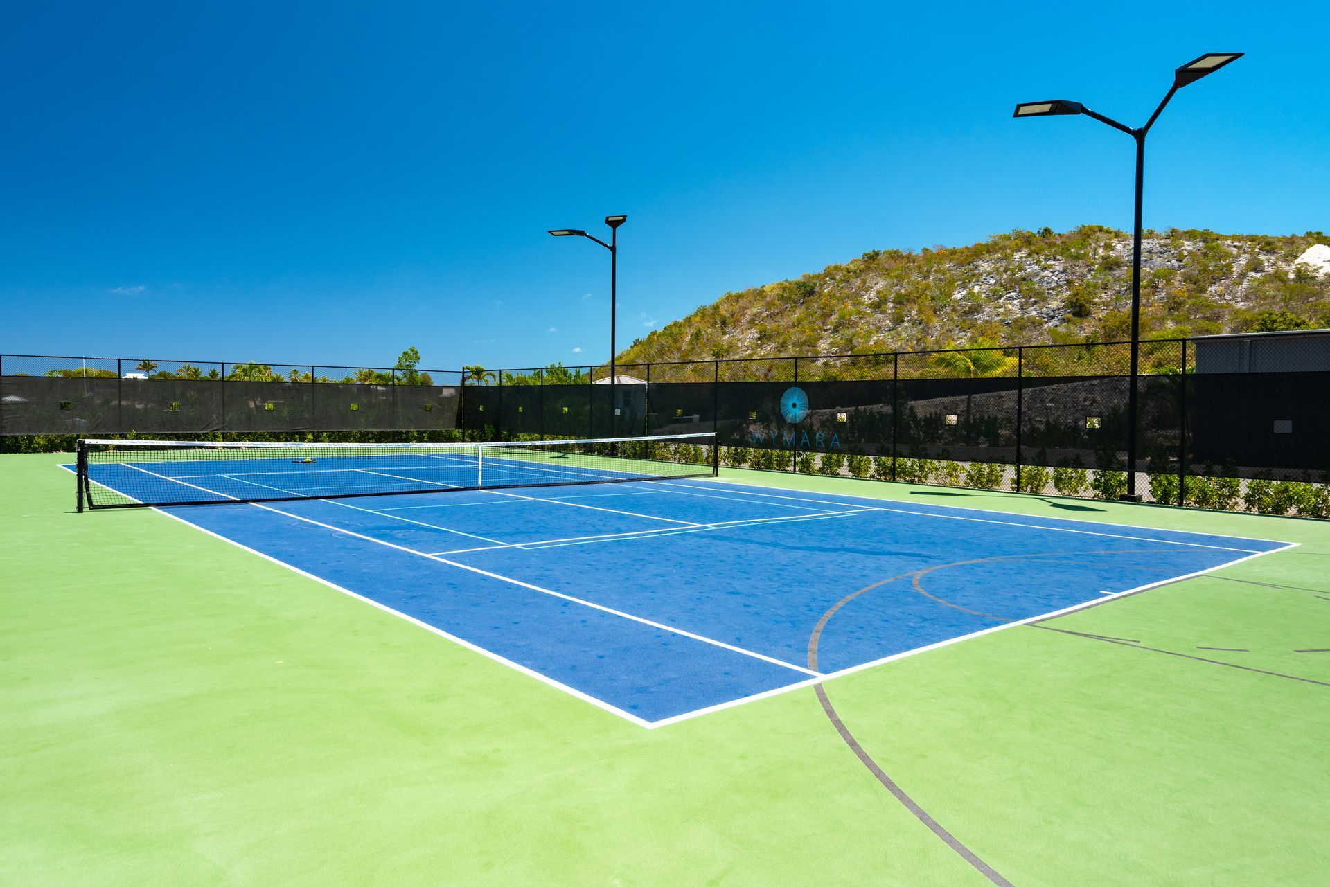 A blue and green tennis court with a black fence
