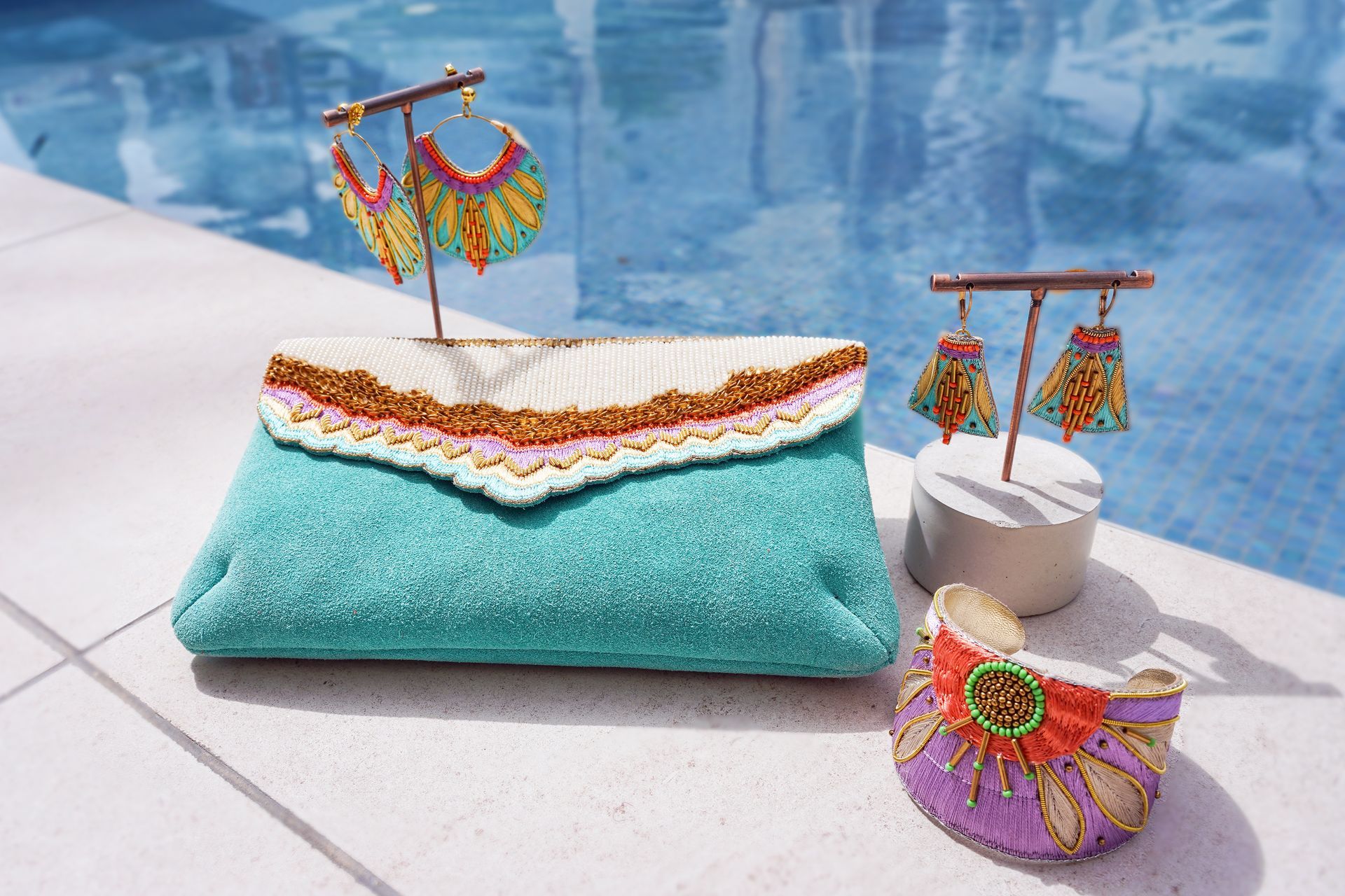 A purse earrings and a bracelet are on display by a pool