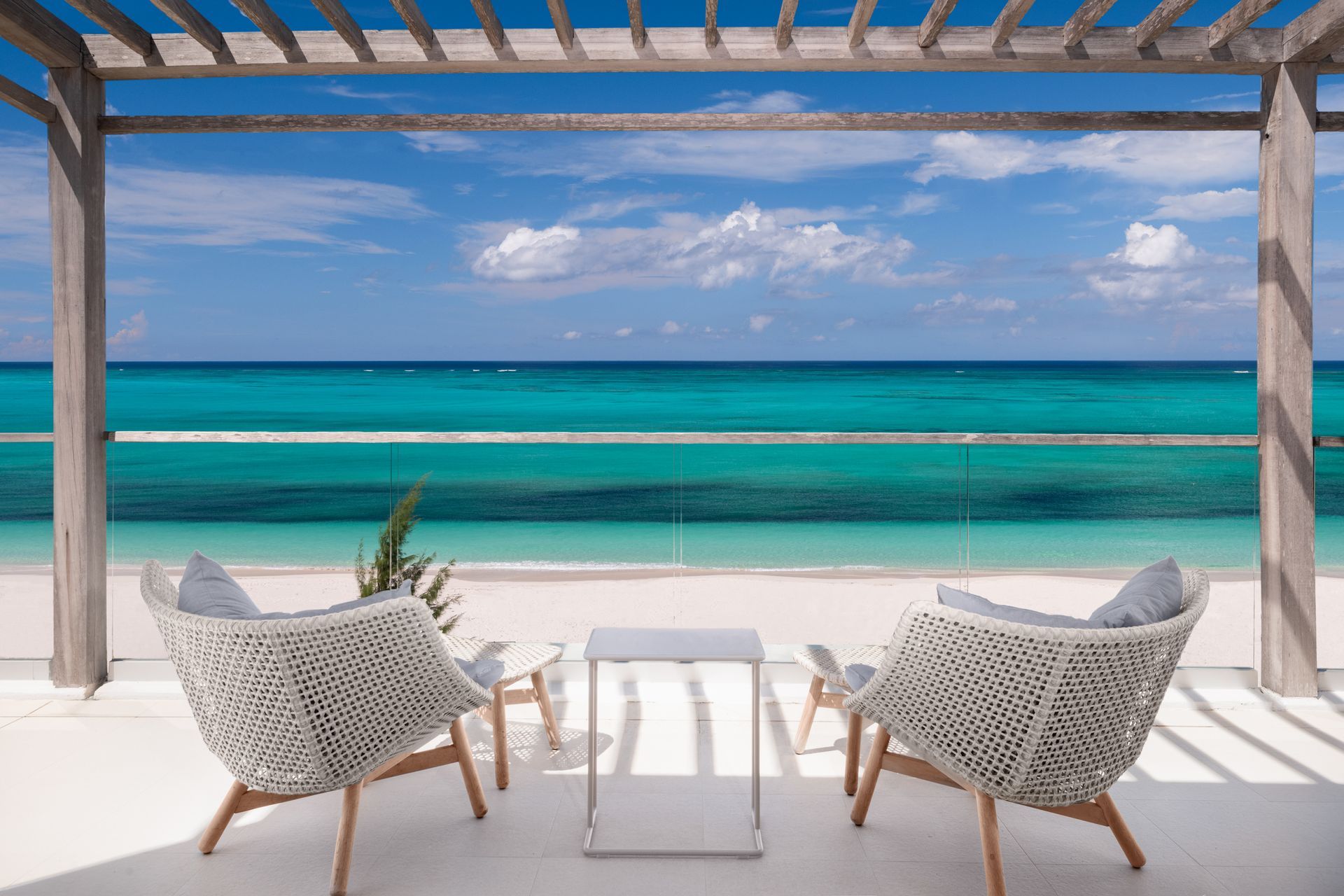 Two chairs and a table under a pergola overlooking the ocean