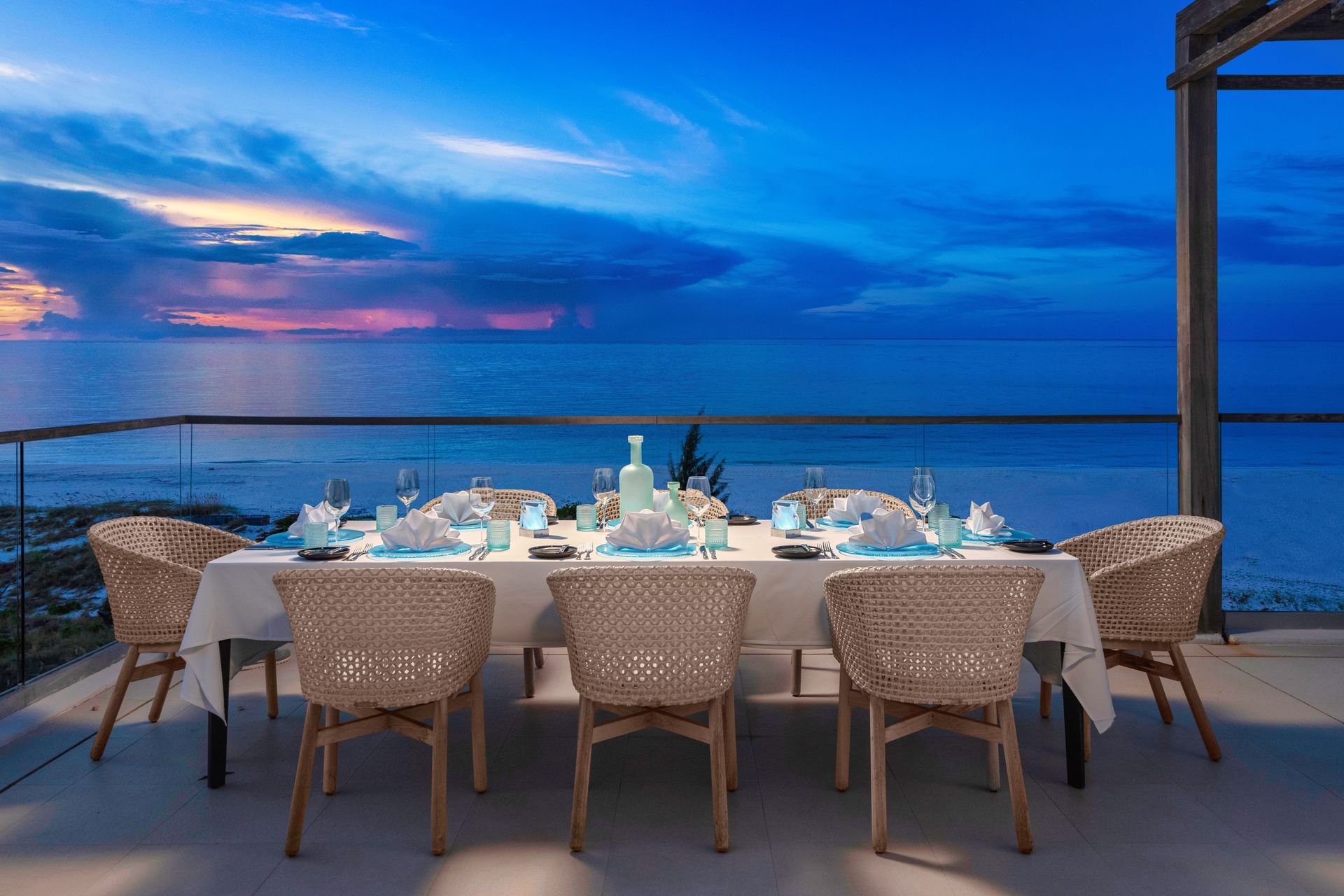 A dining table with wicker chairs and a view of the ocean