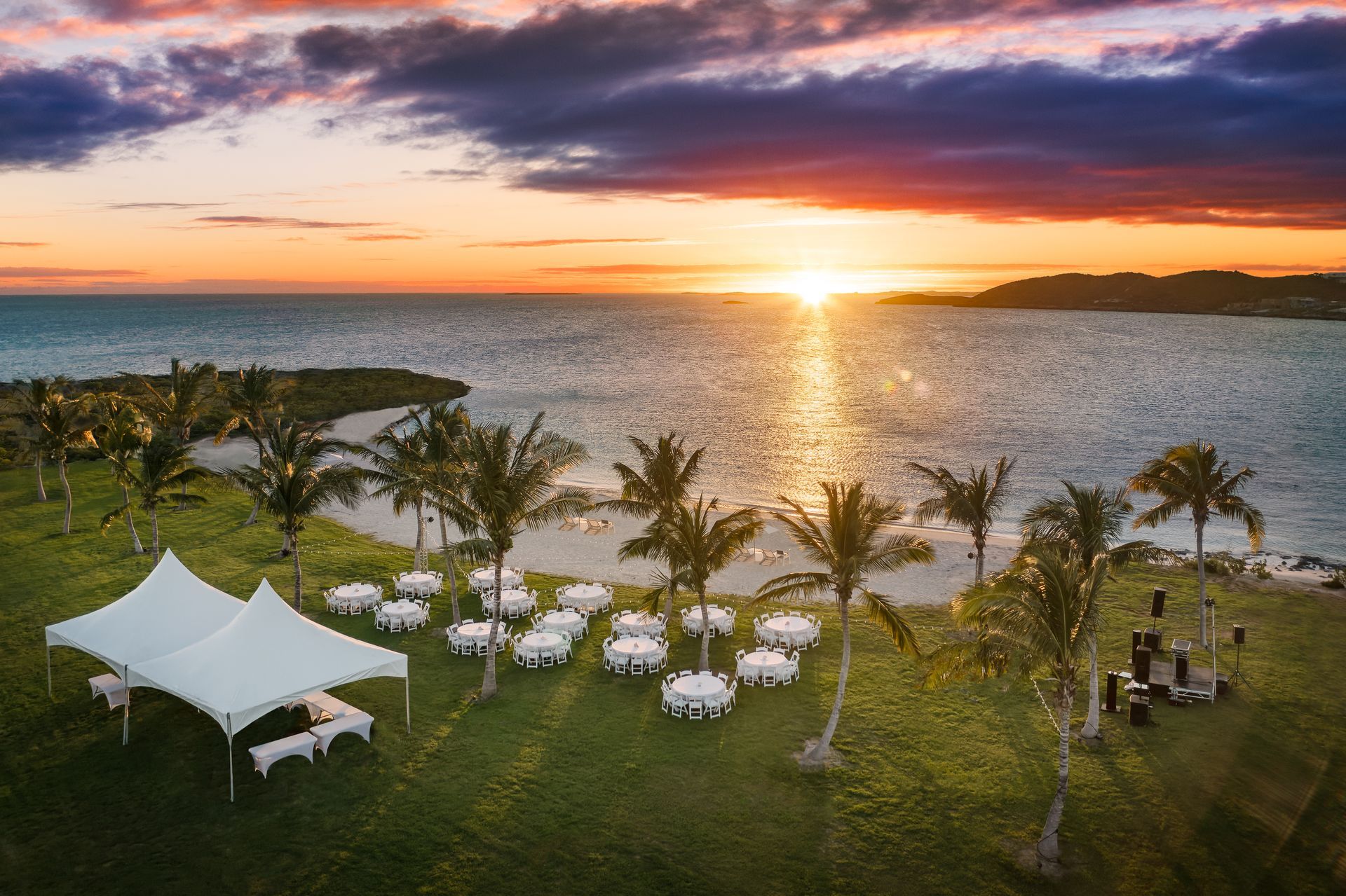 A sunset over the ocean with tables and tents in the foreground
