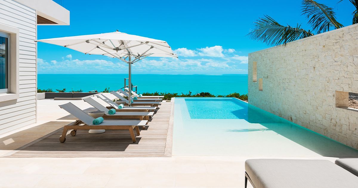 A swimming pool with chairs and umbrellas and a view of the ocean