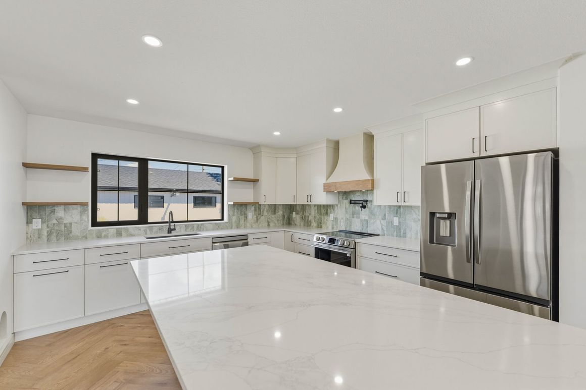 Bright modern kitchen with white island, stainless steel refrigerator, and large window over the sink