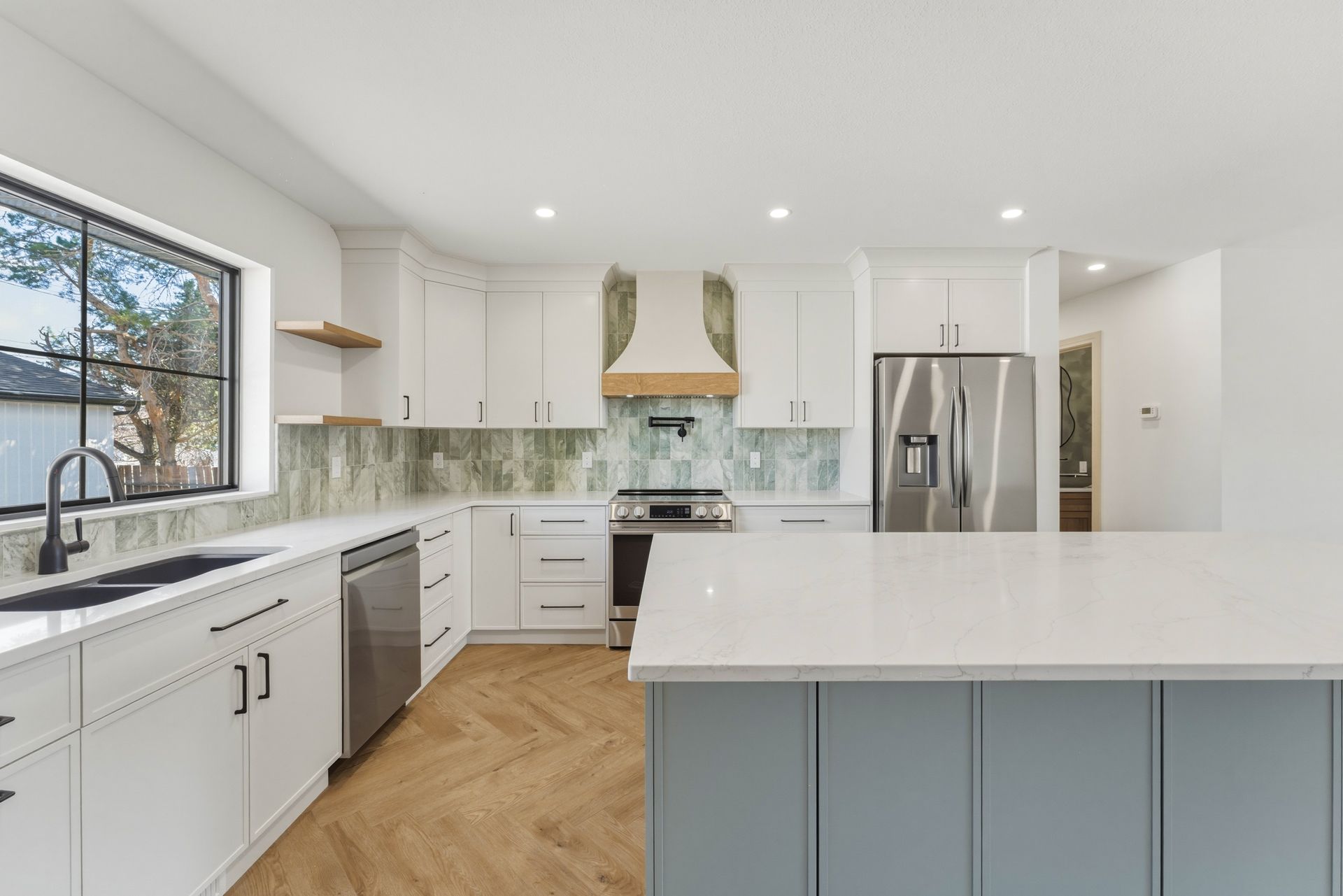 Bright modern kitchen with white cabinets, stainless appliances, herringbone wood floor, and large island