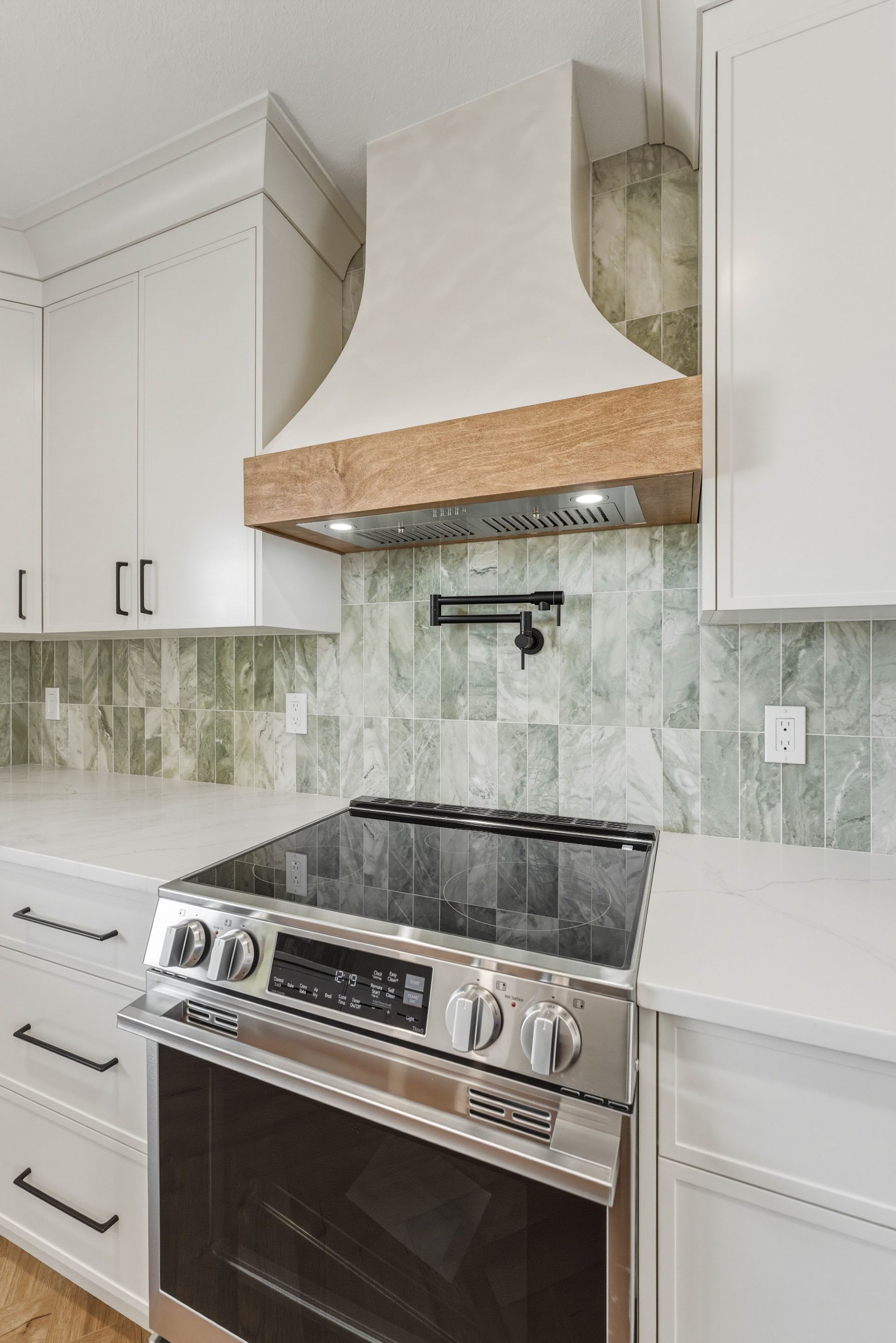 Modern kitchen with white cabinets, green tile backsplash, and stainless steel range under a range hood
