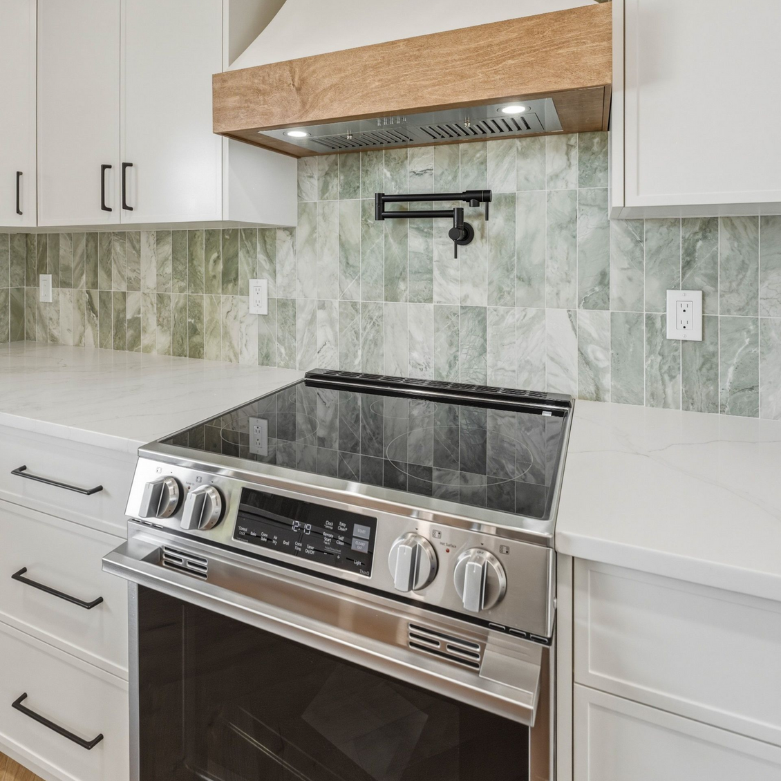 Modern kitchen with stainless steel range, white cabinets, and green marble backsplash