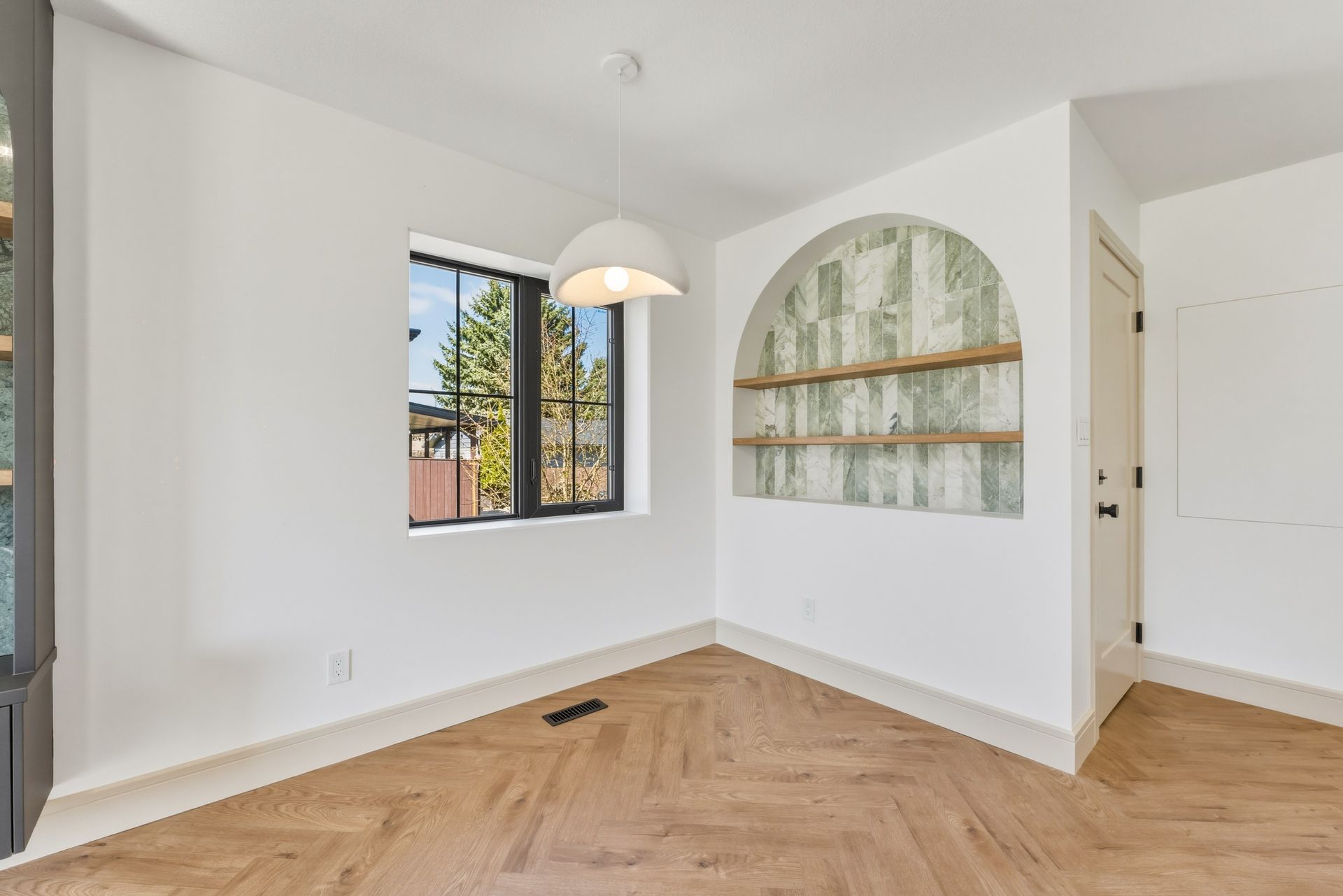 Empty modern room with white walls, herringbone wood floor, window, and arched wall niche.