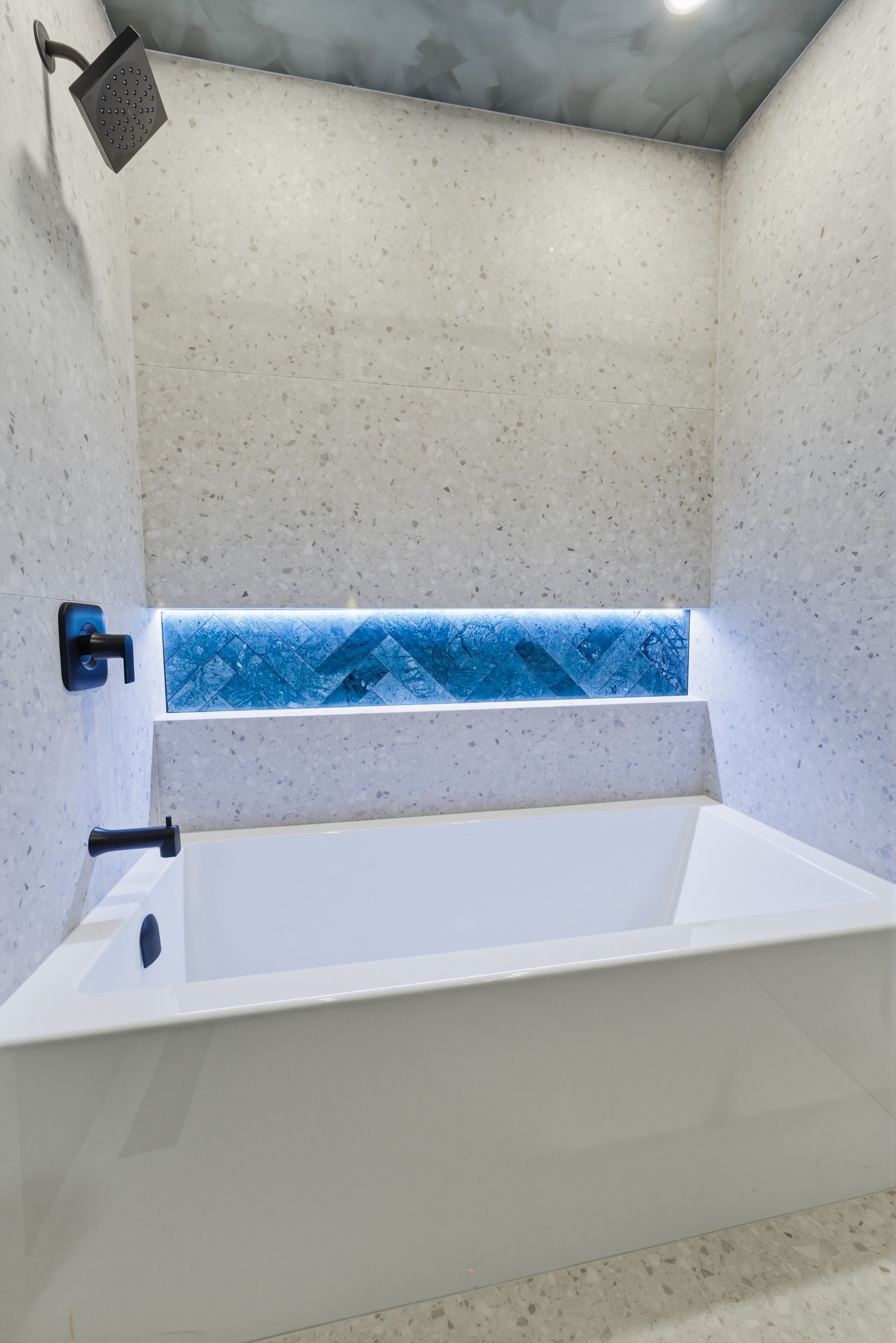 Modern white bathroom with a freestanding tub beneath a blue-lit window nook