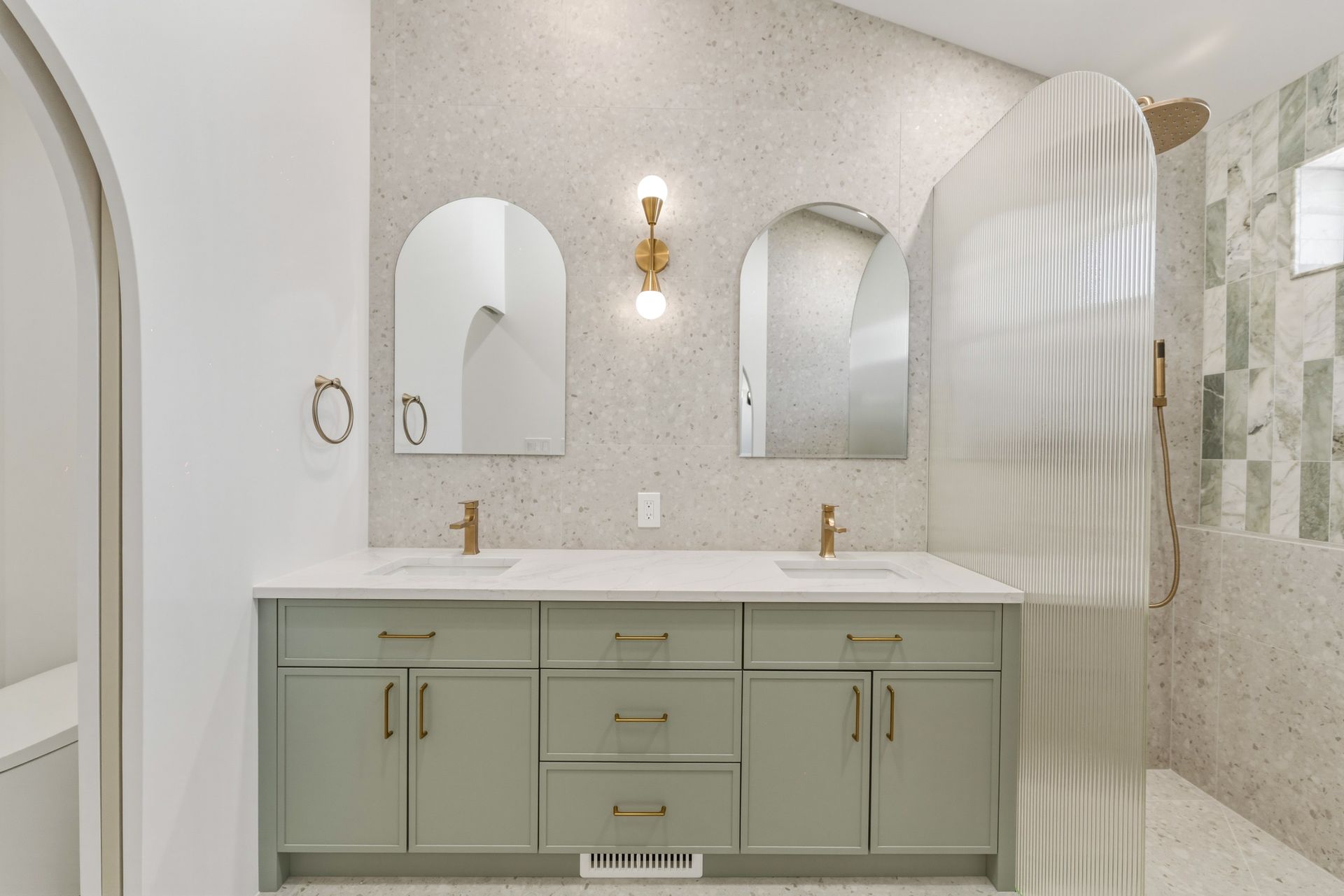 Modern bathroom vanity with double sinks, arched mirrors, and a glass shower enclosure