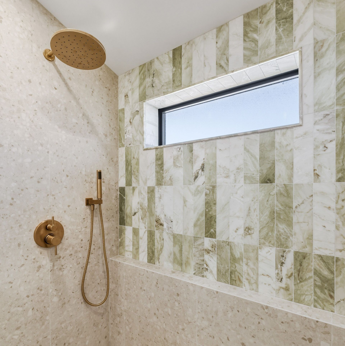 Modern shower with beige stone walls, gold fixtures, and a small horizontal window