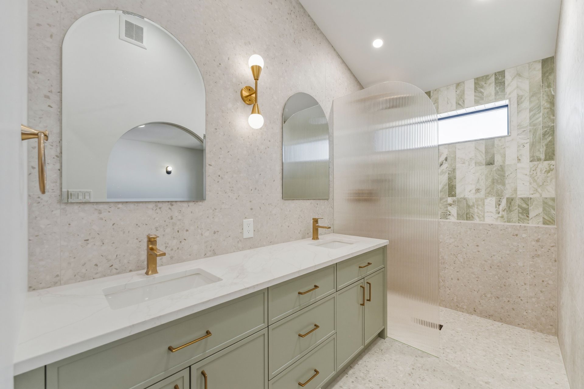 Bright modern bathroom with double vanity, arched mirror, brass fixtures, and walk-in shower