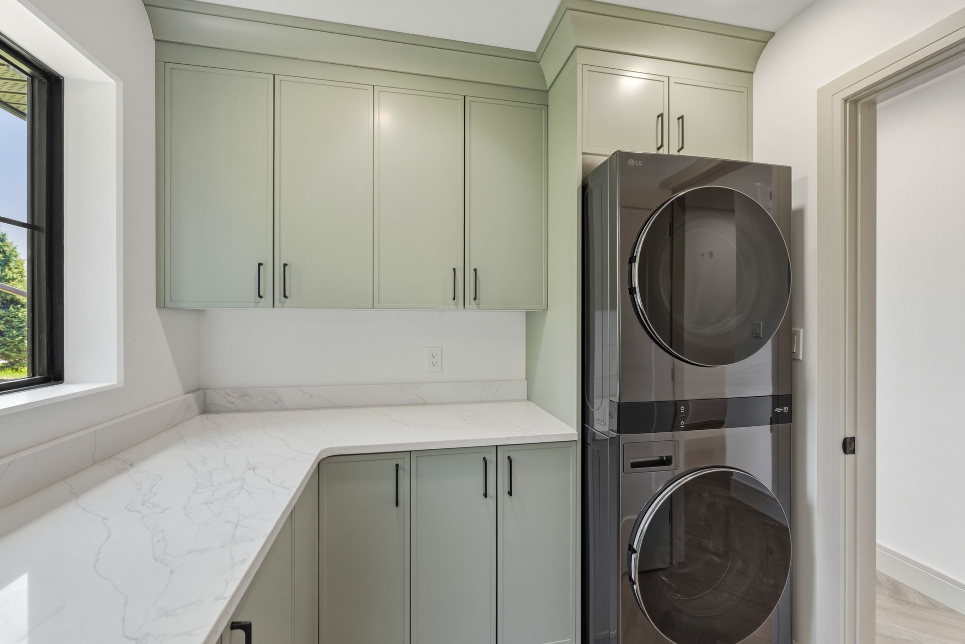 Small laundry room with sage green cabinets, white countertops, and stacked front-loading washer and dryer.