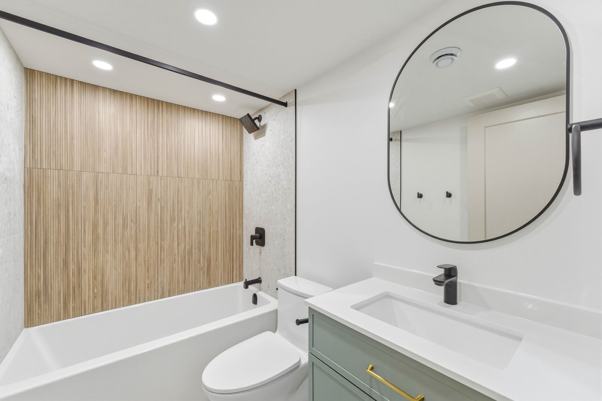 Modern white bathroom with tub, vanity, round mirror, and wood accent wall.