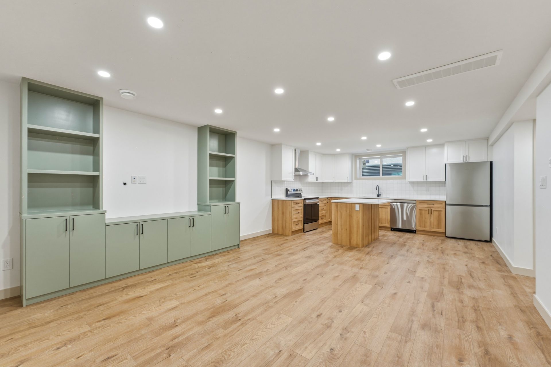 Bright modern kitchen with light wood floors, white walls, green cabinets, and a central island.