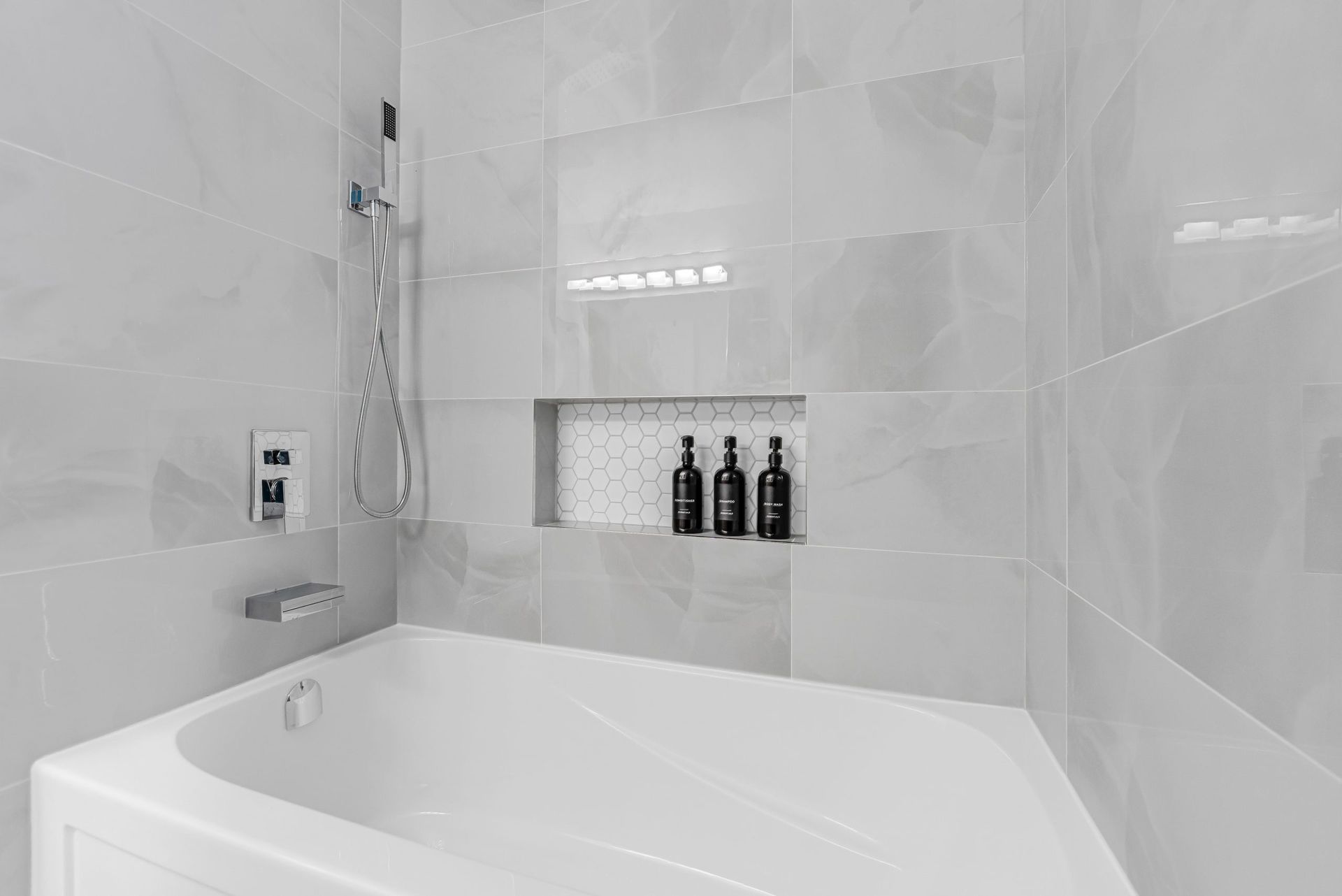 Modern white bathroom with a bathtub, tiled walls, and built-in shelf holding bottles