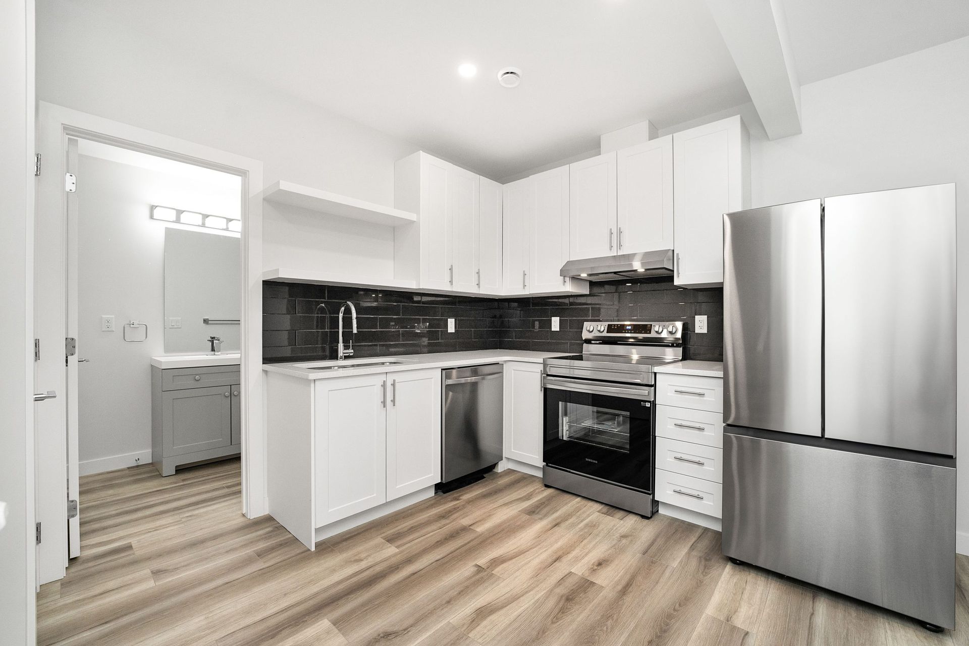 Modern white kitchen with black backsplash, stainless steel appliances, and wood-look flooring
