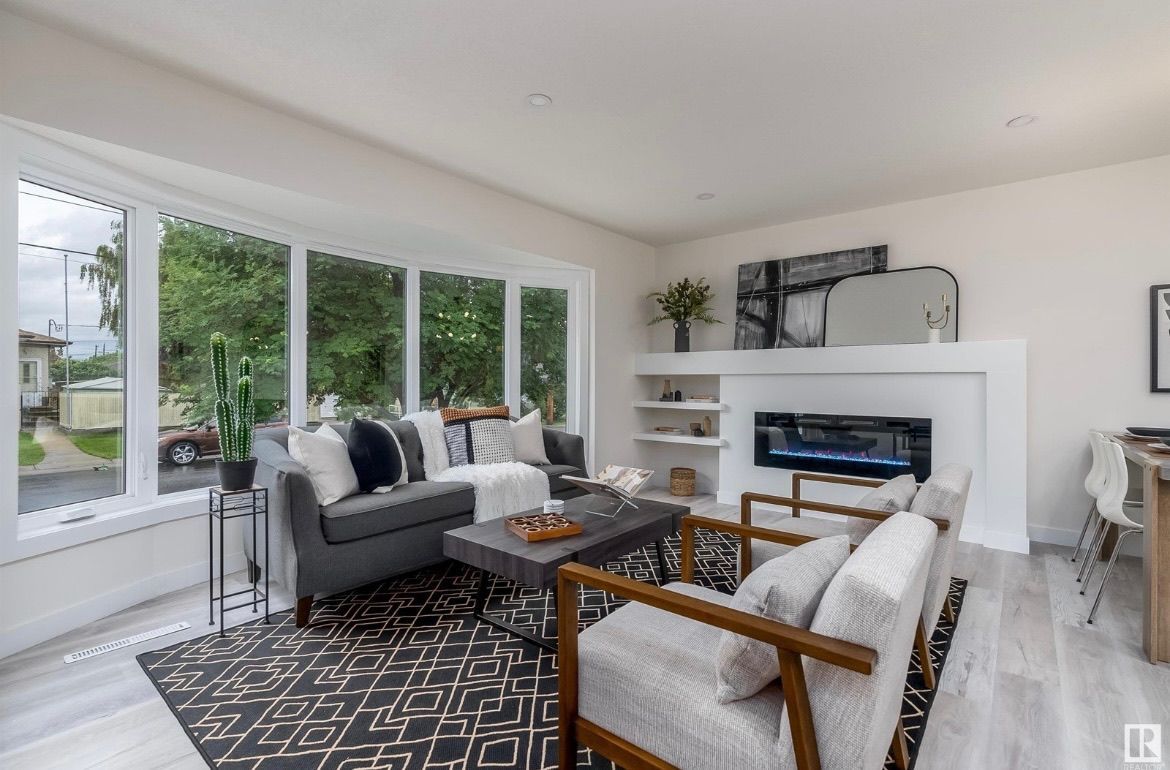 Bright modern living room with gray sofa, patterned rug, white fireplace, and large windows