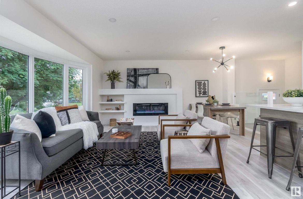 Bright modern living room with gray sofa, black patterned rug, fireplace, and kitchen bar stools
